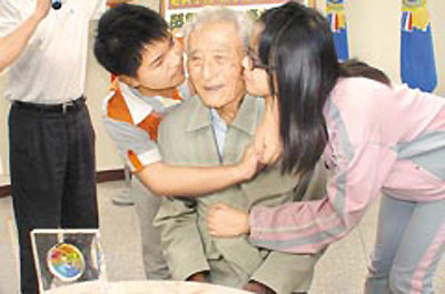 荣眷遗孤天使─胡寿宏老伯伯20日捐出新台币500万元股票结余款，长期受他认养升学的何奕轩右、陈焜文左2感动地回报拥抱与亲吻。图片来源：台湾《中国时报》